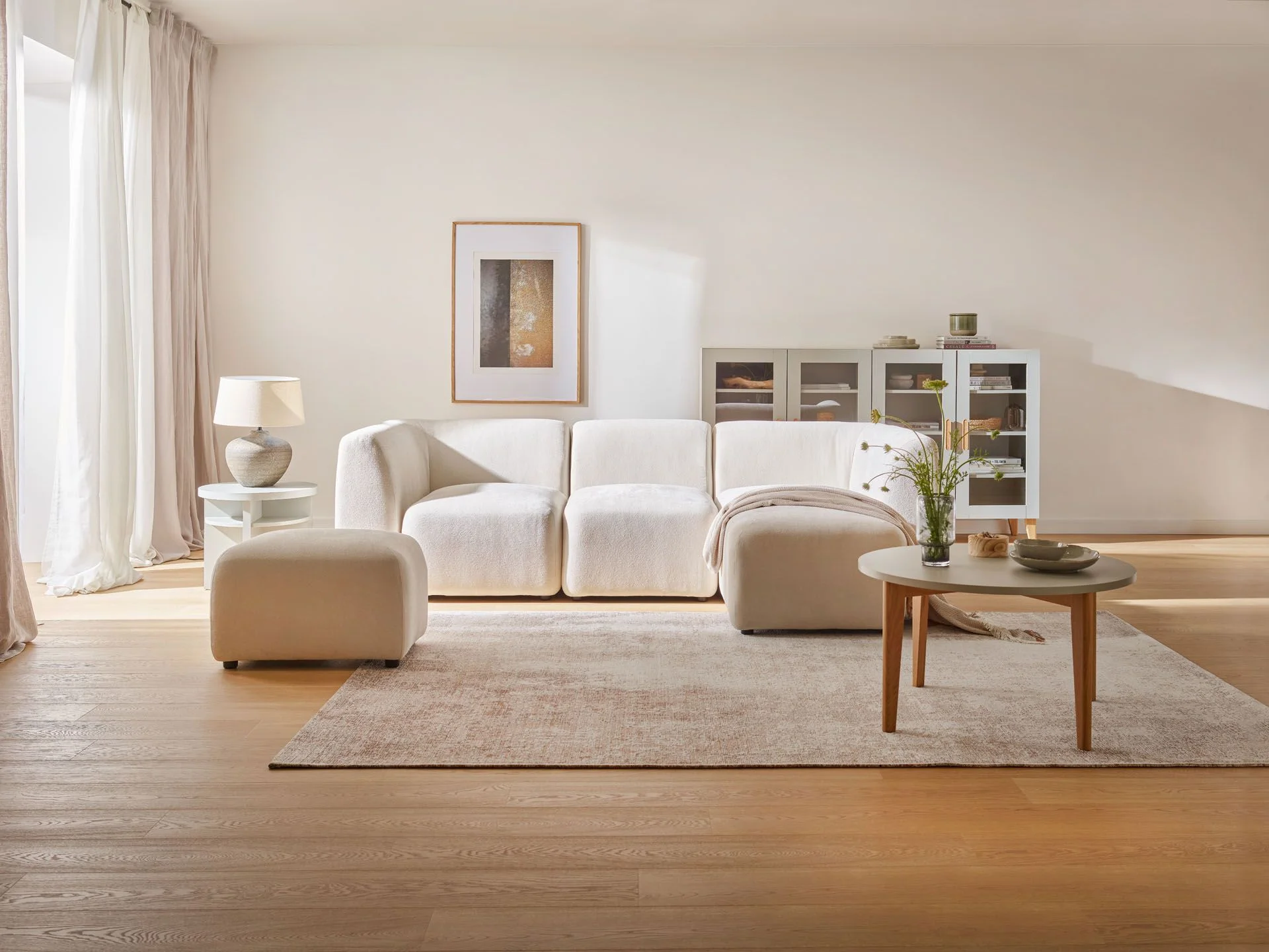 Minimalistyczny salon z miękką, białą sofą, jasnym dywanem i subtelnymi dodatkami w naturalnej kolorystyce.